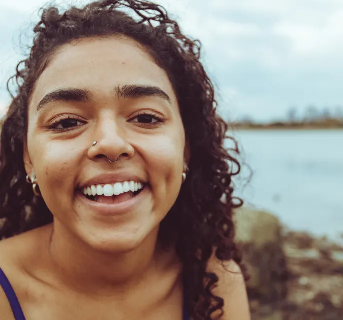 Jovem de cabelo cacheado sorrindo à beira de um lago