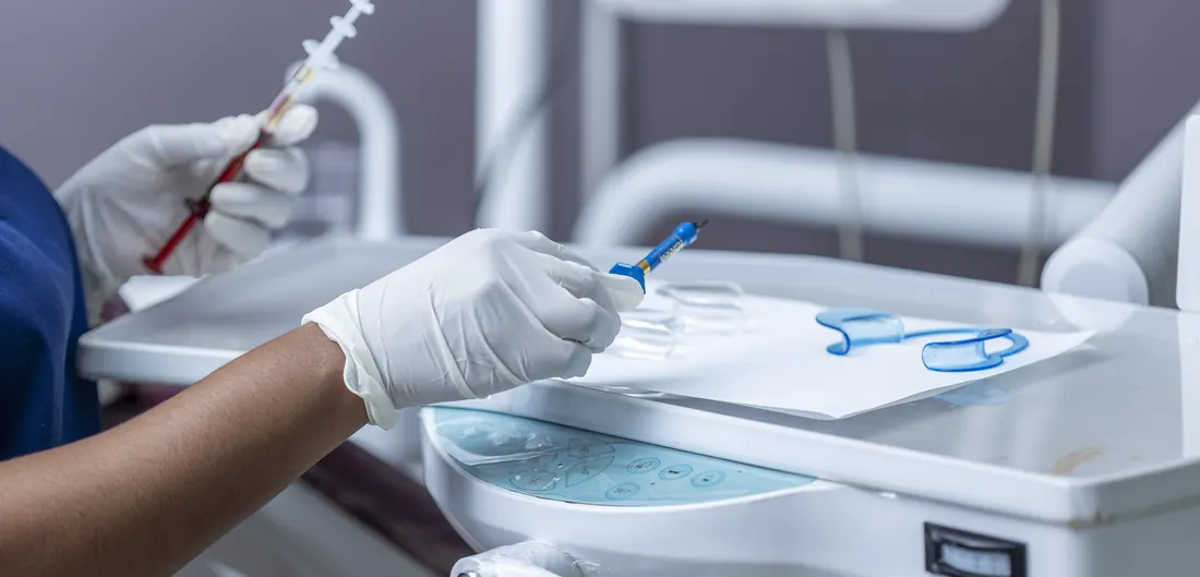 Mãos de luvas organizando instrumentos odontológicos numa bandeja ao lado da cadeira