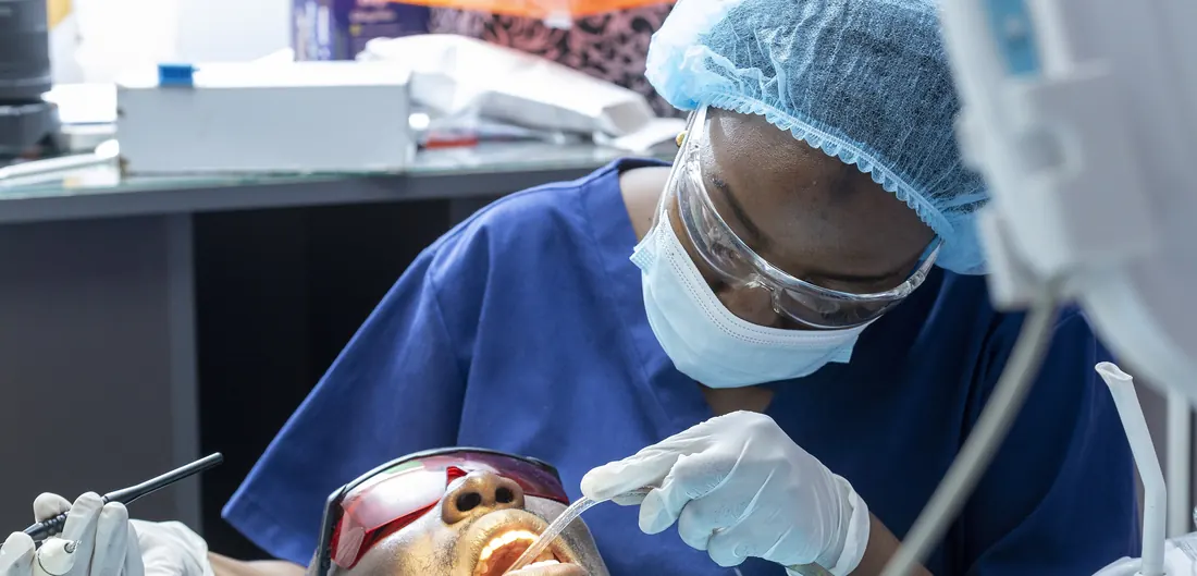 Dentista de máscara e óculos de proteção tratando um paciente na cadeira