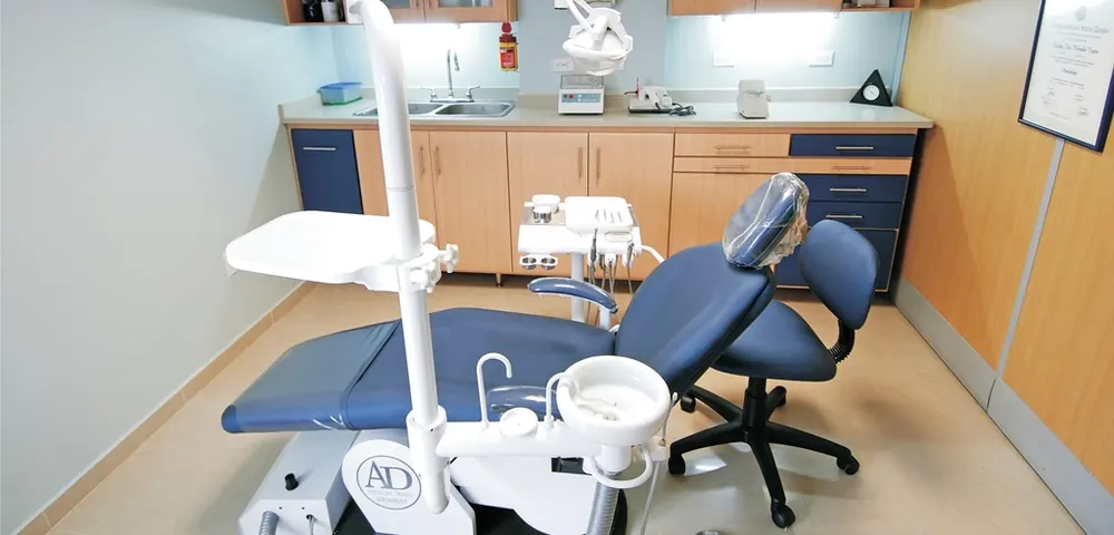 Consultório claro com cadeira odontológica azul e armários de madeira