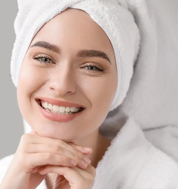 Mulher com toalha no cabelo sorrindo, com a mão no queixo